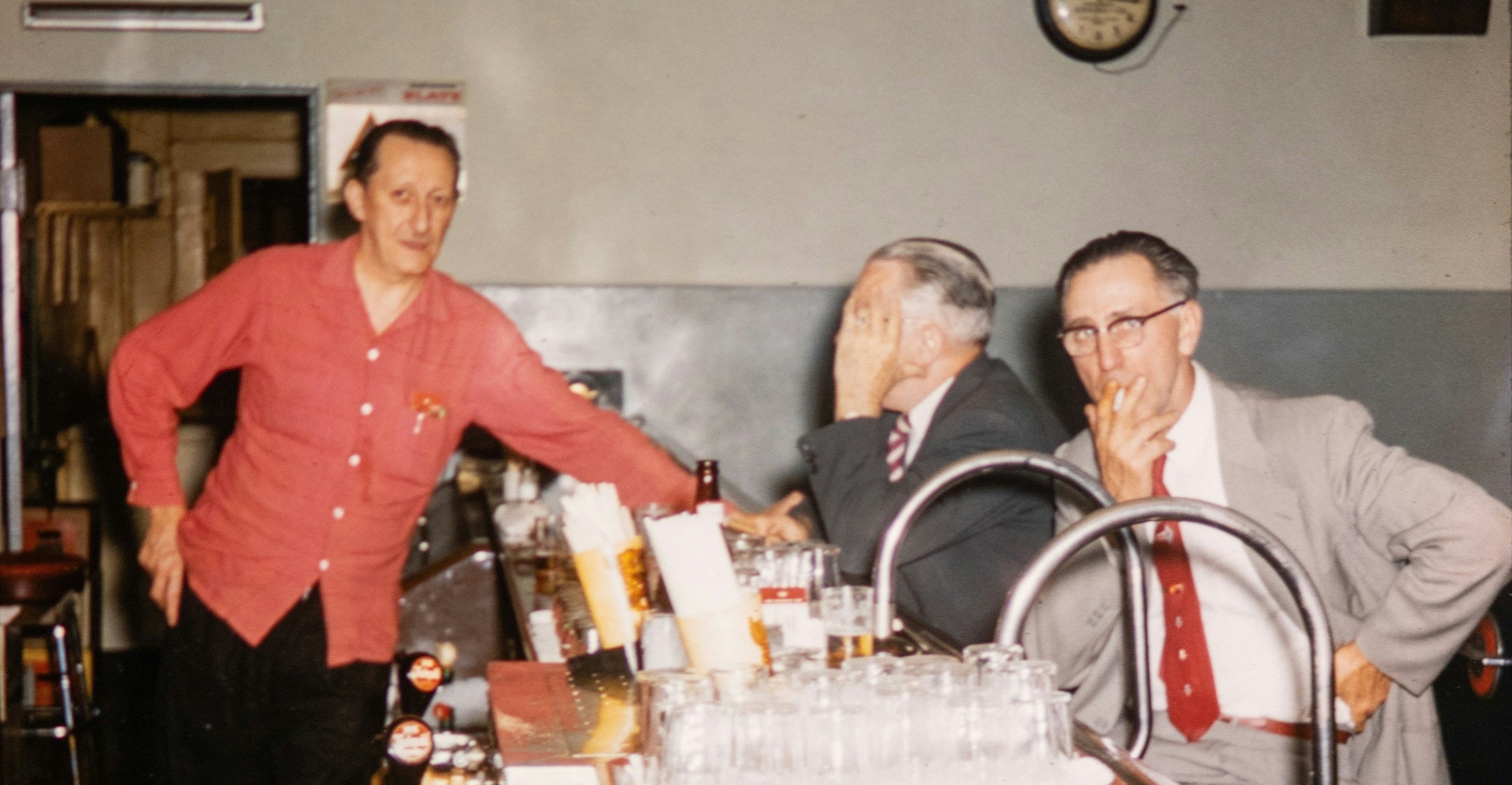 Three men at a bar counter with a clock on the wall.